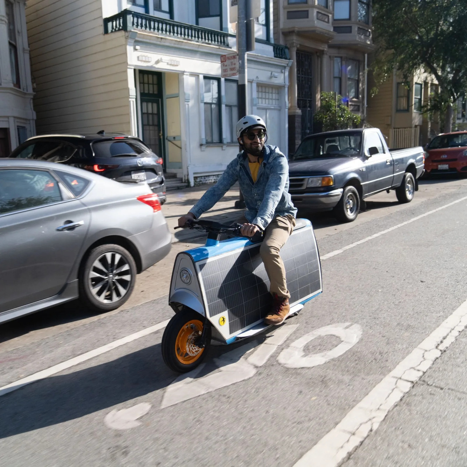 A rider in a white helmet on a Smile Machine in a San Francisco bike lane, passing parked cars and Victorian houses